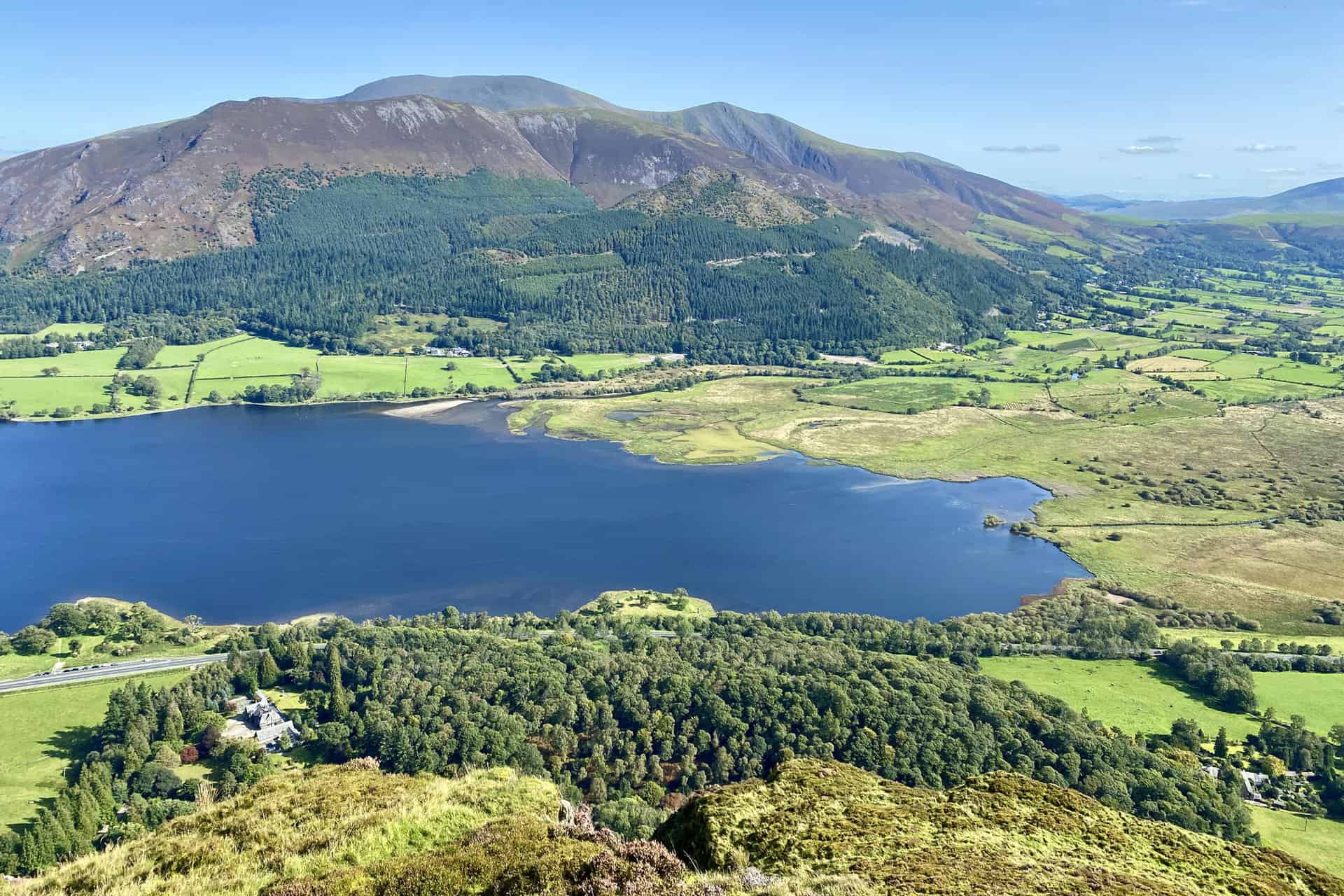 The southern extent of Bassenthwaite Lake and a few of the northern fells as seen from the summit of Barf. The smaller, tree-covered hill on the other side of the lake is Dodd. Behind Dodd are the peaks of Carl Side, Long Side and Ullock Pike. At the back are the summits of Little Man and Skiddaw.