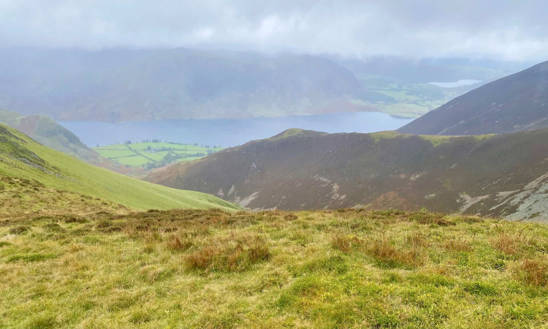 The strong winds blowing over Whiteless Edge momentarily clear the mist to reveal Crummock Water and Mellbreak. Loweswater is also visible in the distance on the right.