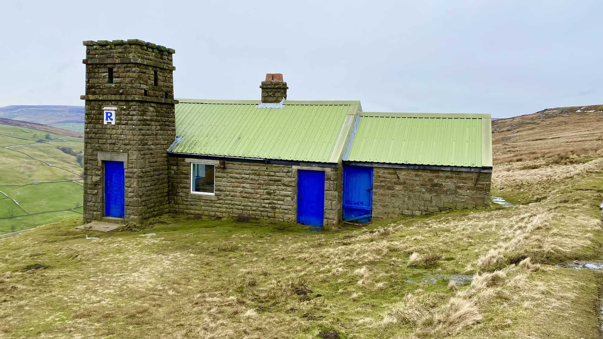 The shooting house above Thrope Edge on Lofthouse Moor, its bright green corrugated roof and vivid blue doors striking against the natural hues of the countryside.