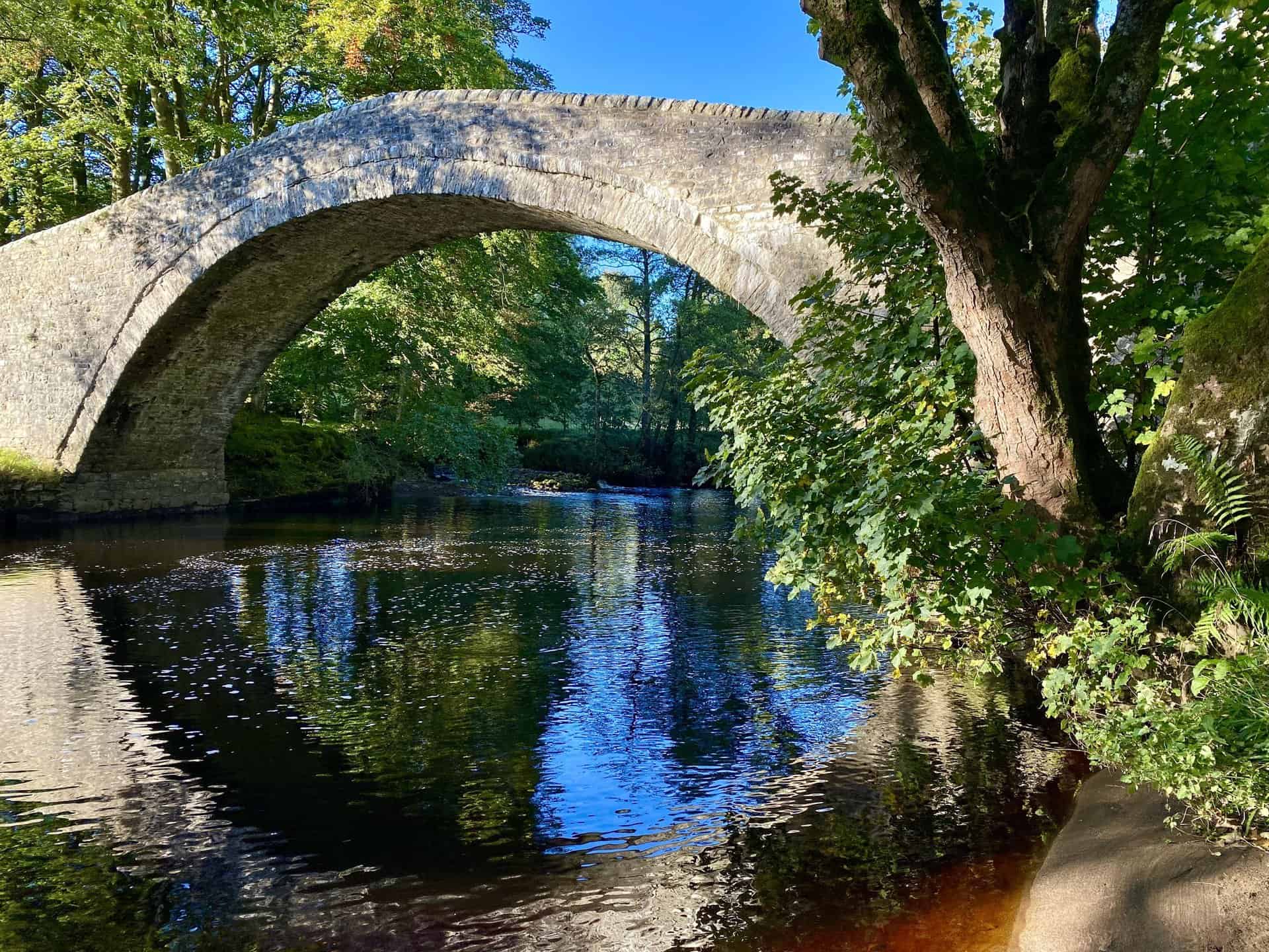 The picturesque Ivelet Bridge gracefully arches over the River Swale in Swaledale, North Yorkshire. Just a stone's throw from the quaint village of Gunnerside, its ancient stones are beautifully illuminated by the sunlight.