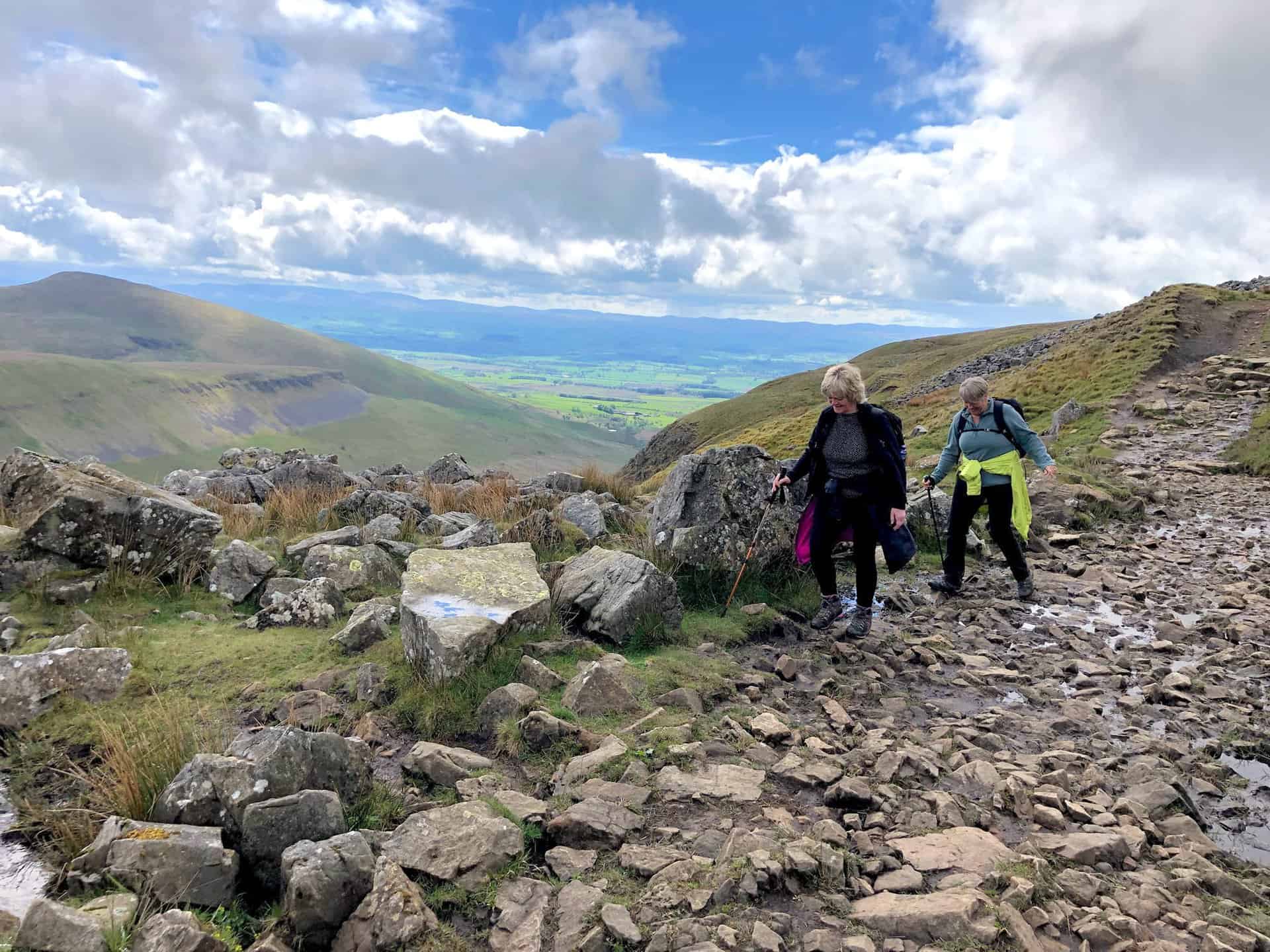 A rocky section of the Pennine Way, with the hills of the Yorkshire Dales visible on the horizon. Navigating this rocky terrain adds a sense of adventure to the High Cup Nick walk.