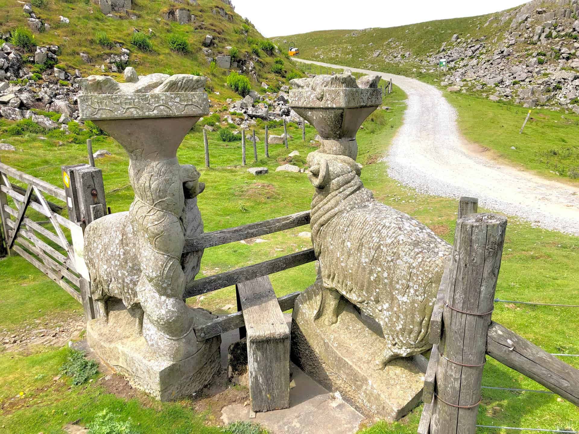 Intricately crafted stone sheep flank a stile near Holwick Scars, blending art with the natural landscape.
