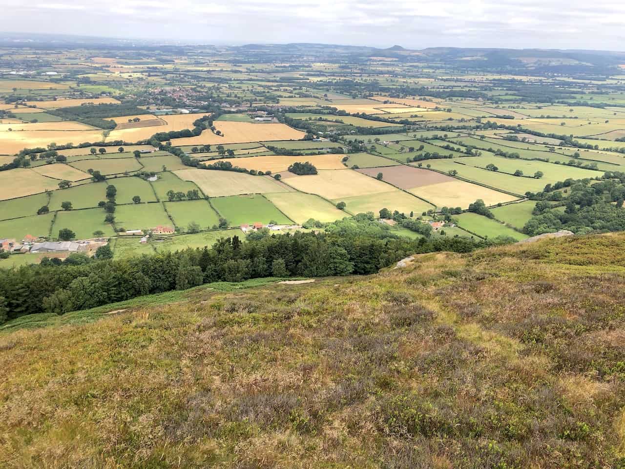From the northward view along the Cleveland Way on Cold Moor, the distinctive shape of Roseberry Topping emerges on the horizon, to the right of centre. The charming village of Great Broughton nestles in the landscape's top third, on the left.