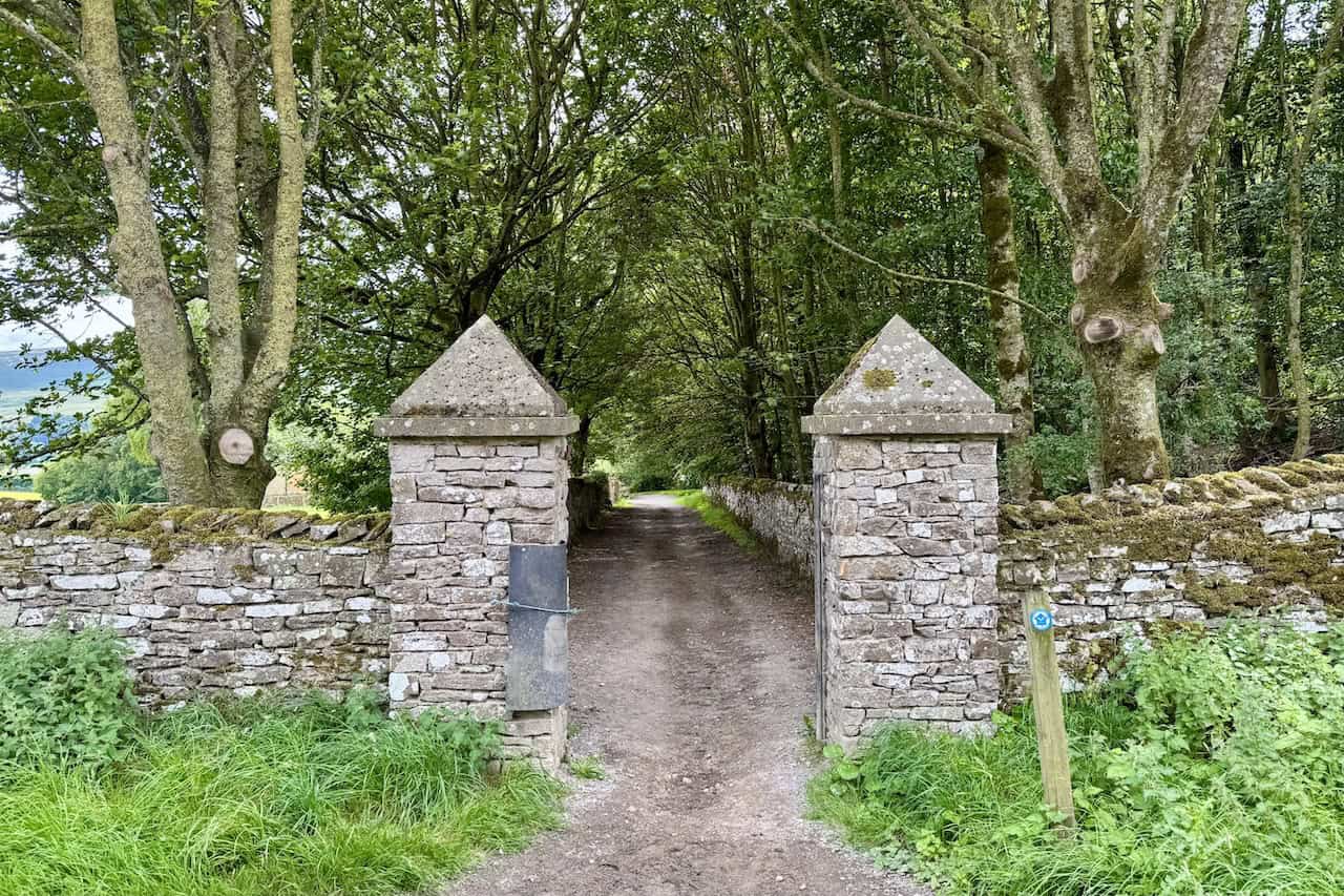 A pair of stone gateposts marks the entrance into shady woodland.
