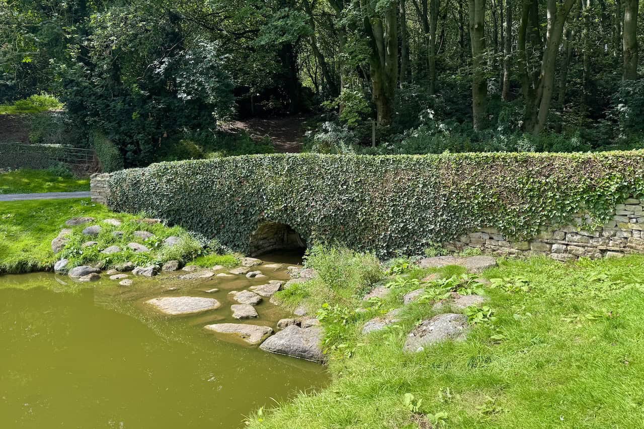 A stone bridge crosses a stream flowing into ornamental ponds.
