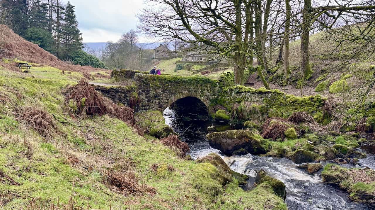 A walker crossing the beautiful moss-covered stone-arched bridge over Hebden Beck on the Grassington circular walk, close to the hamlet of Hole Bottom.