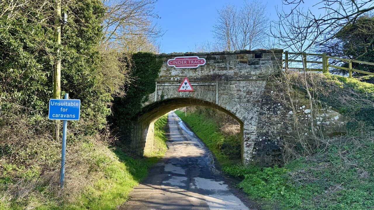 Stone bridge carrying the Cinder Track over Field Lane at the start of the Cloughton Wyke walk, with the tarmac lane leading north-east towards Cliff Top House.