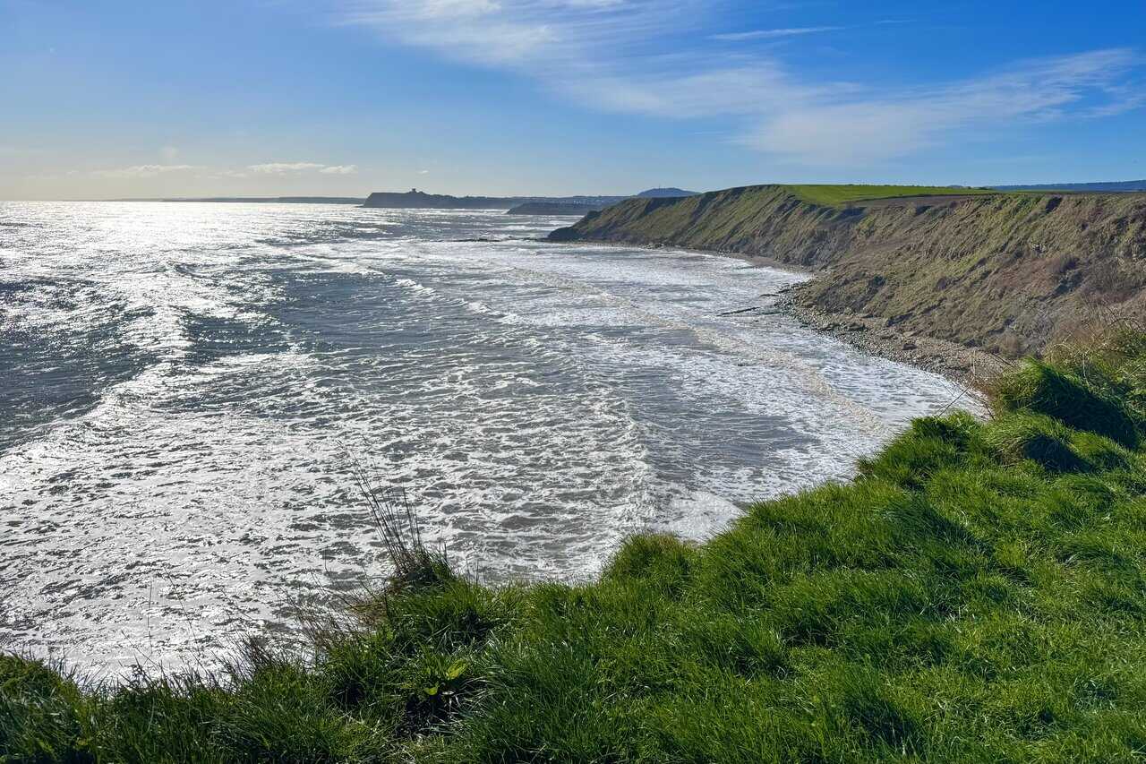 Southward coastal view towards Scarborough on the Cloughton Wyke walk, with Scarborough Castle faintly visible on the headland above the town and bays.
