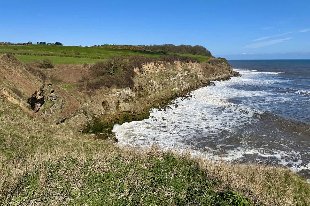 View down into Cloughton Wyke inlet, where a small stream runs through a cliff gully to the boulder-strewn shore below.
