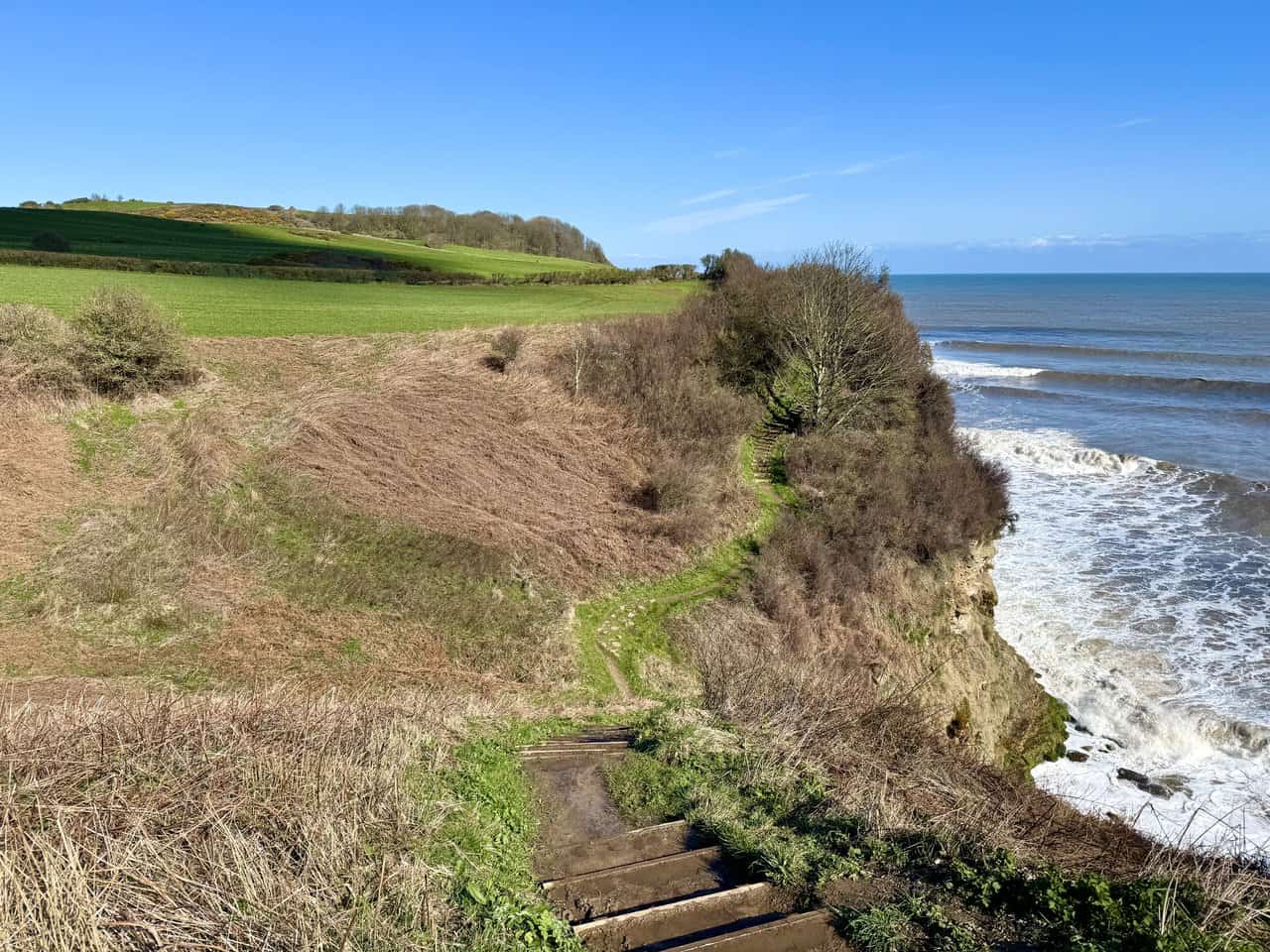 Wooden steps dropping and rising around the head of Cloughton Wyke on the Cloughton Wyke walk, with open sea to one side and farmland inland.