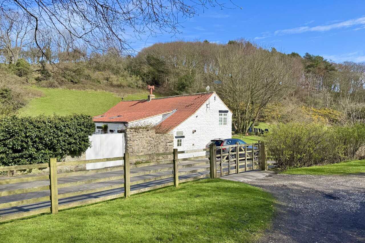 White-washed cottage in Newlands Dale with a red pantile roof and an old-style warning plaque fixed to the fence.