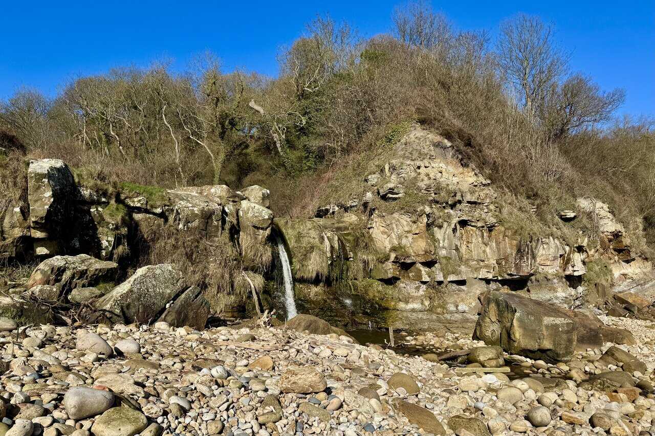 Small waterfall where Hayburn Beck cascades onto Hayburn Wyke beach among boulders and pebbles.