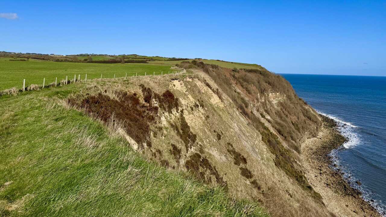 Clifftop path north of Hayburn Wyke, with green fields inland and cliffs dropping to the rocky shore.