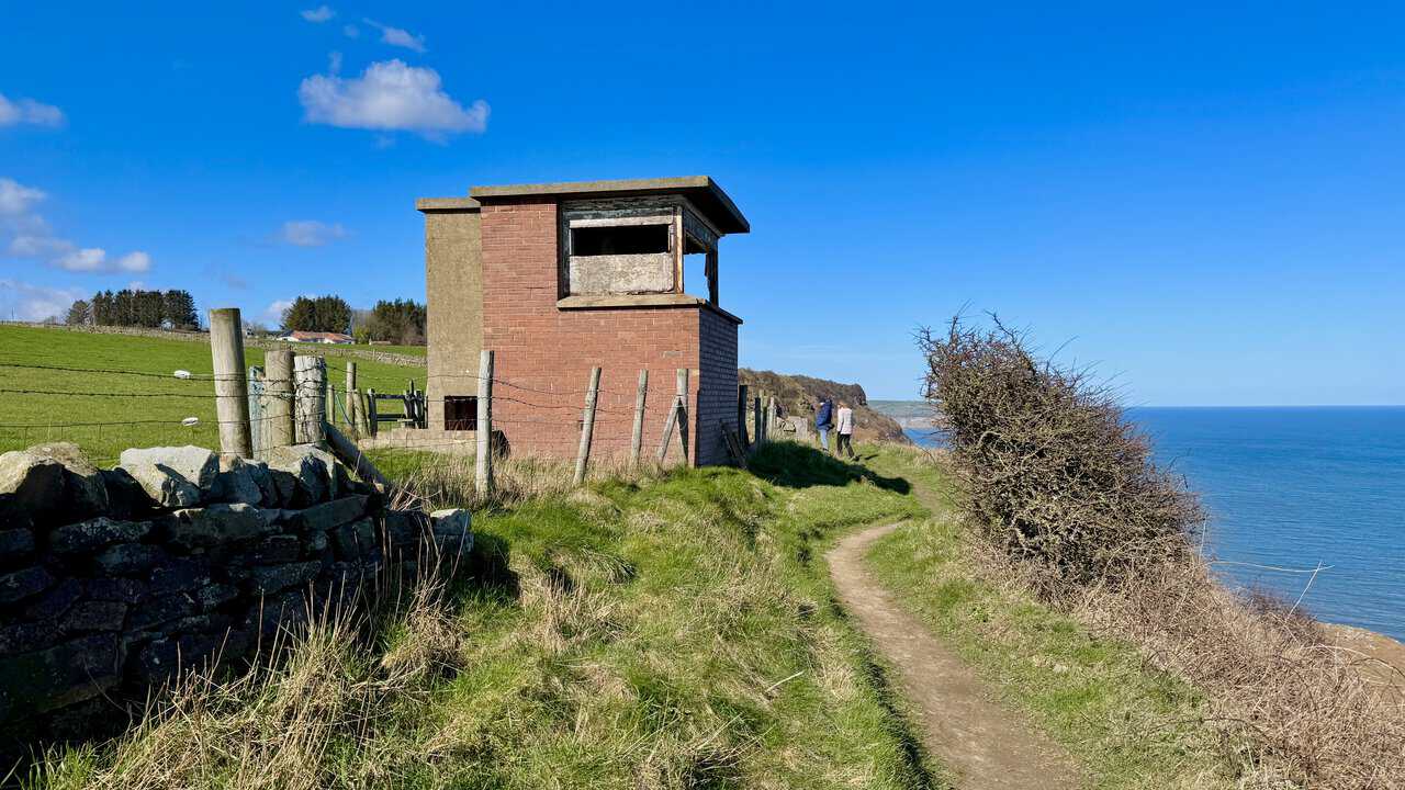 Coastguard Station on the cliff edge, with radar station remains in the field behind.