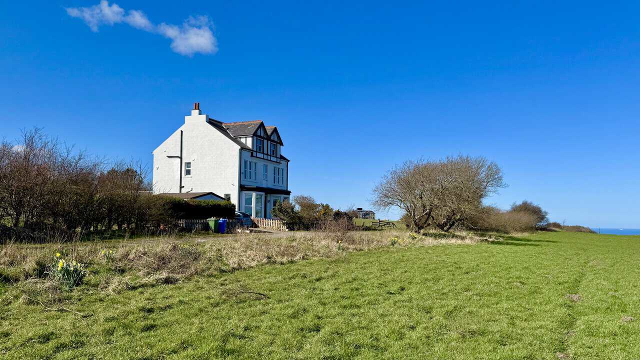 Large white Victorian house standing alone on the clifftop above the sea.