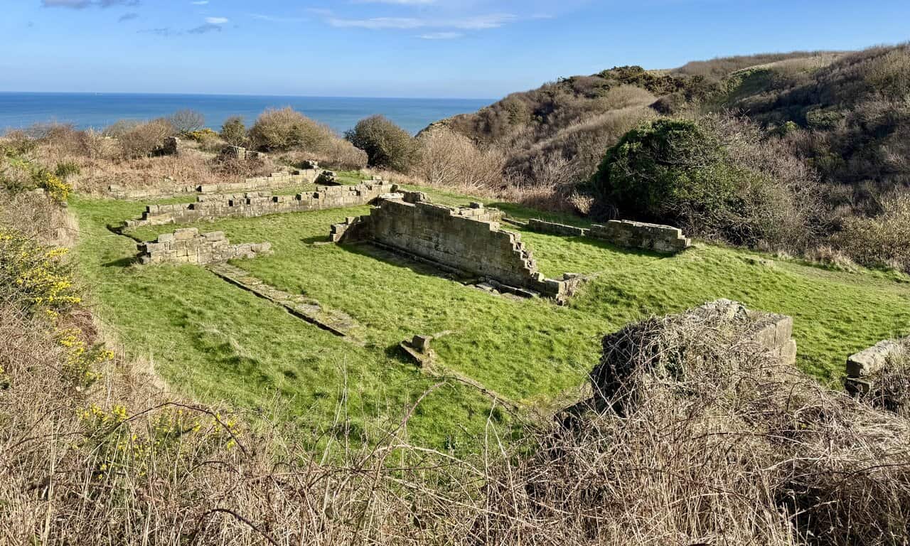 Peak Alum Works today, with preserved ruins, large spoil mounds softened by gorse and scrub, and interpretation boards around the site.