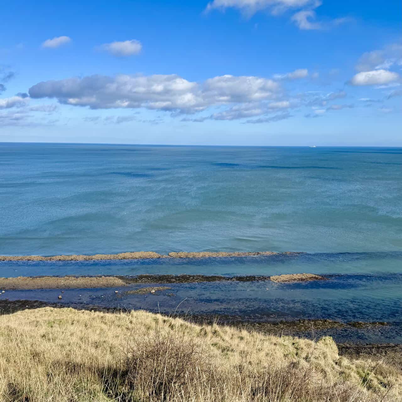 View from above Miller’s Nab, with turquoise and deep-blue sea beyond a broad wave-cut rock platform exposed at low tide.