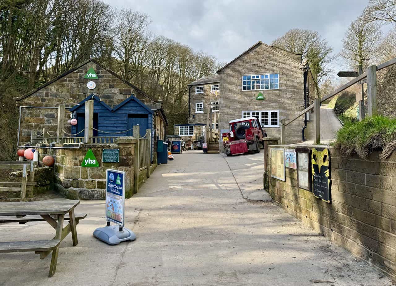 Boggle Hole youth hostel at the foot of a steep wooded ravine, with the converted old mill building beside the beach.