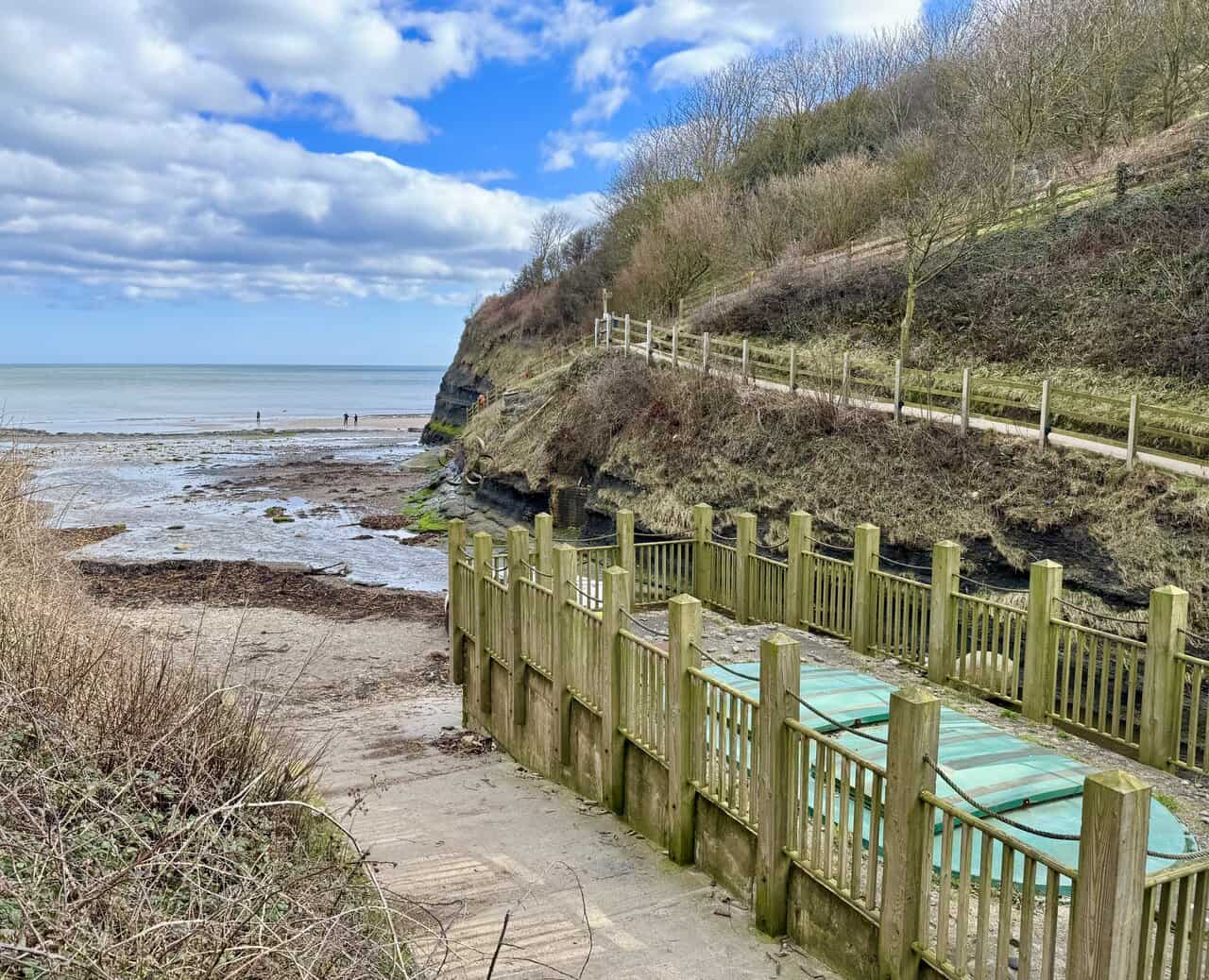 Rocky shoreline at Boggle Hole at low tide, with pools, seaweed and boulders spread across the beach below the cliffs.