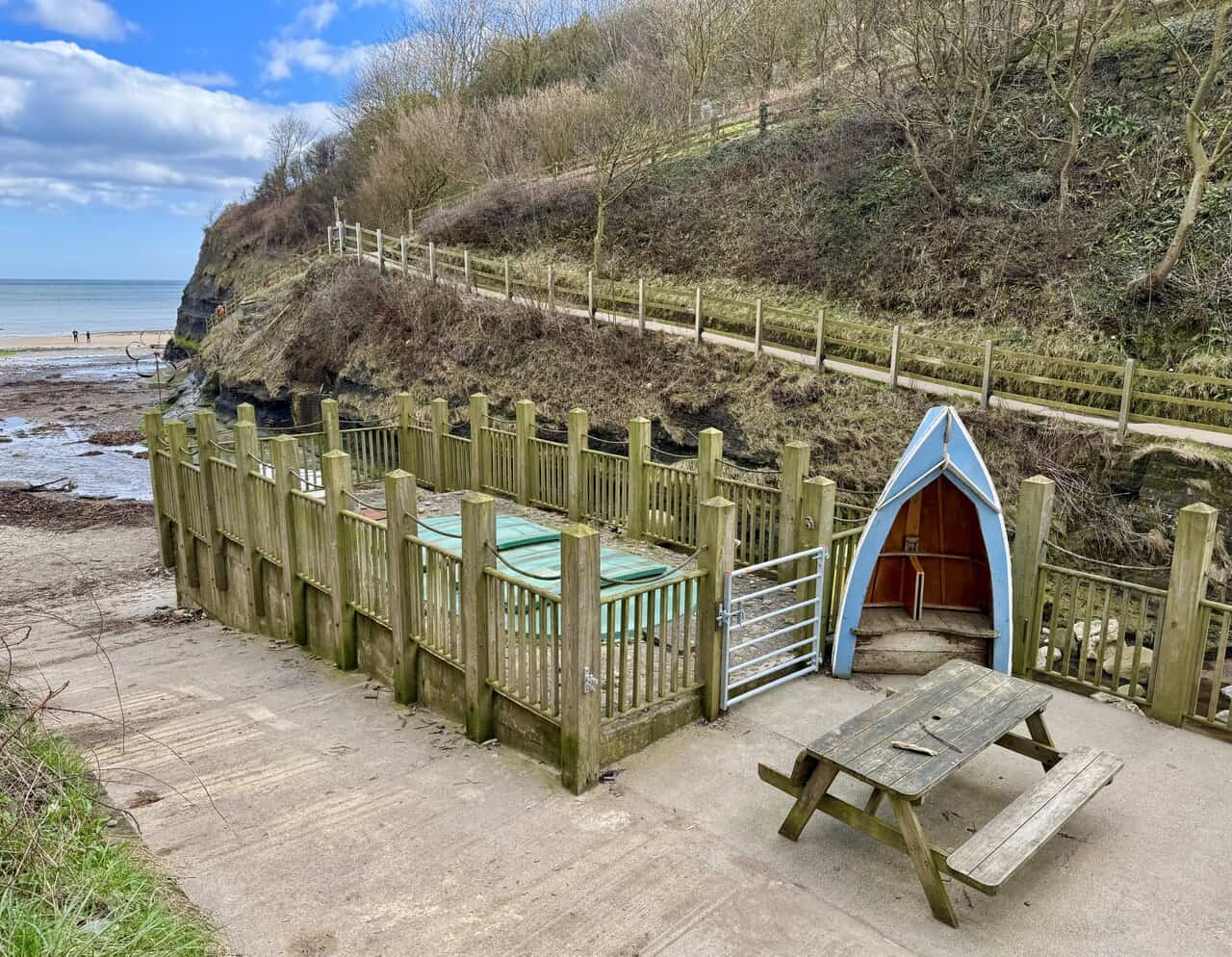 High cliffs above Boggle Hole beach, with a picnic bench and boat-shaped shelter beside the rocky cove.