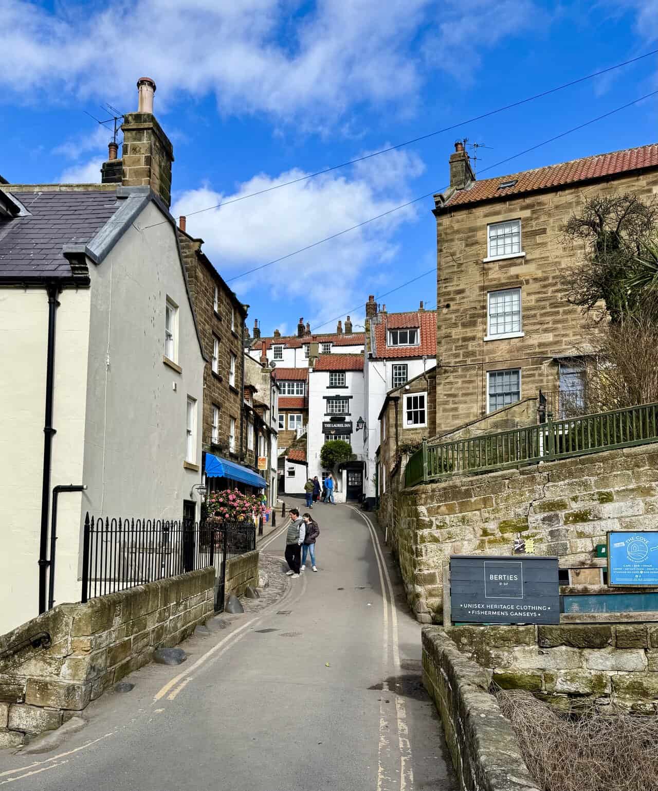 Steep road through Robin Hood’s Bay, with tightly packed buildings, village signs and shops rising up the hill.
