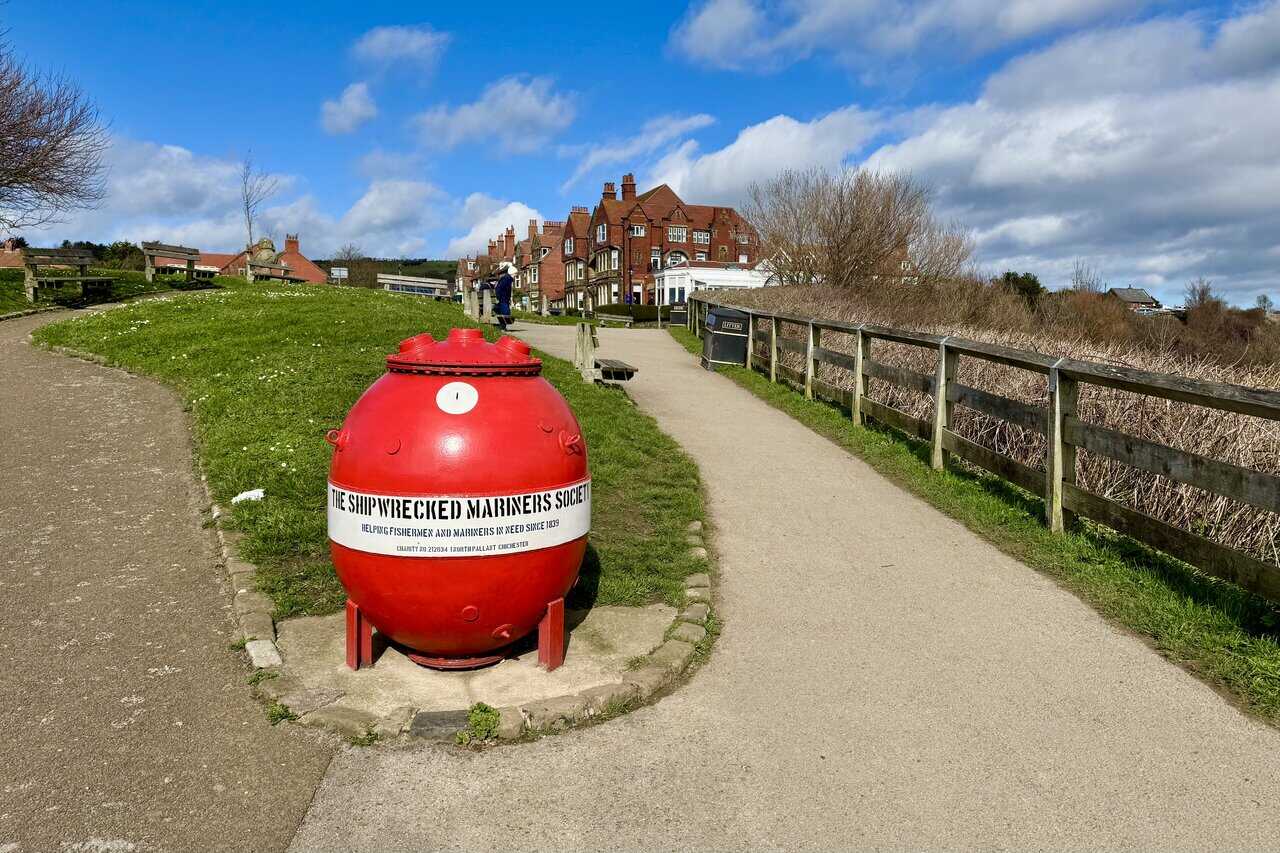 Bright red Shipwrecked Mariners’ Society collection box shaped like a naval mine beside the path at the top of Robin Hood’s Bay.