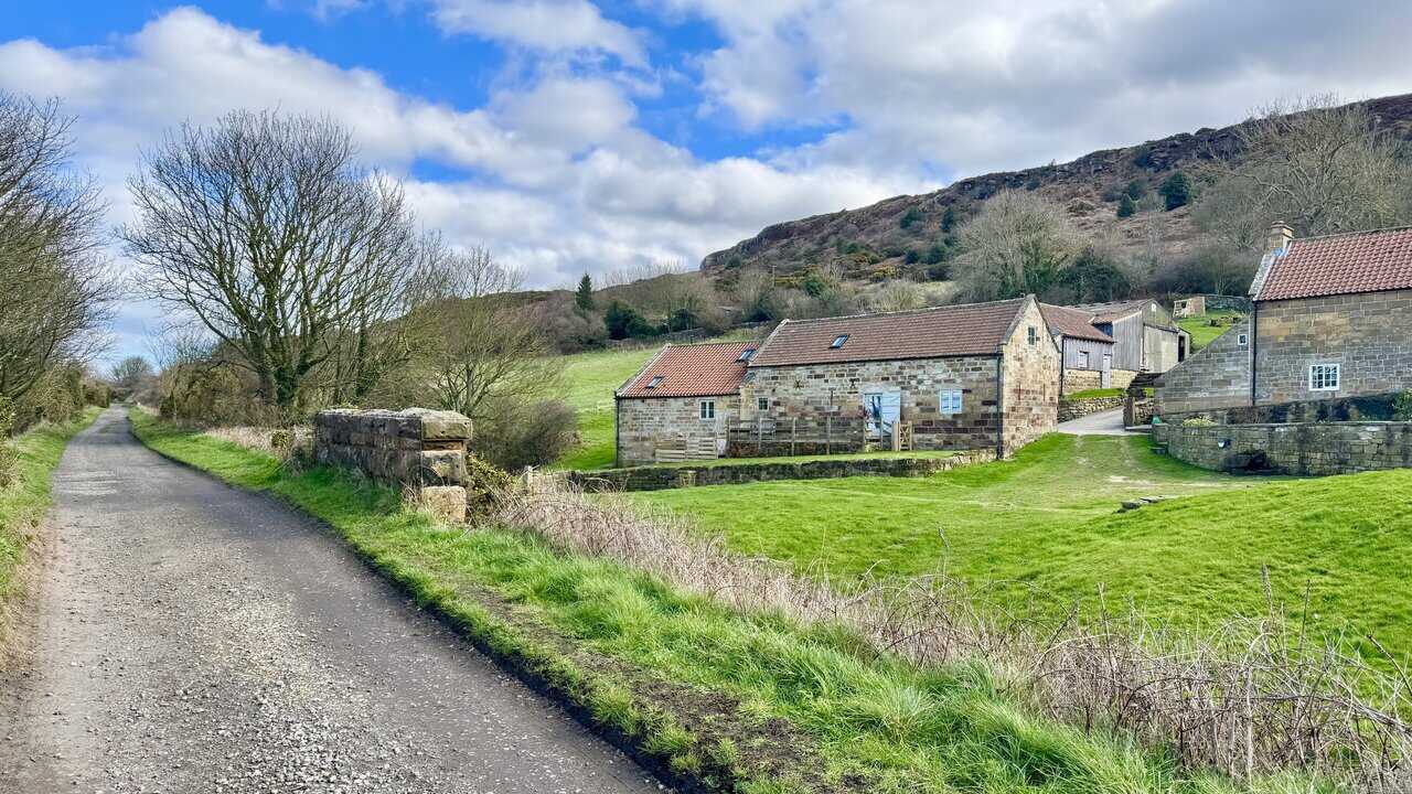 Stoupe Brow Farm beside the Cinder Track, with stone buildings and red pantile roofs beneath the steep hillside. This is about three-quarters of the way round the Ravenscar walk.