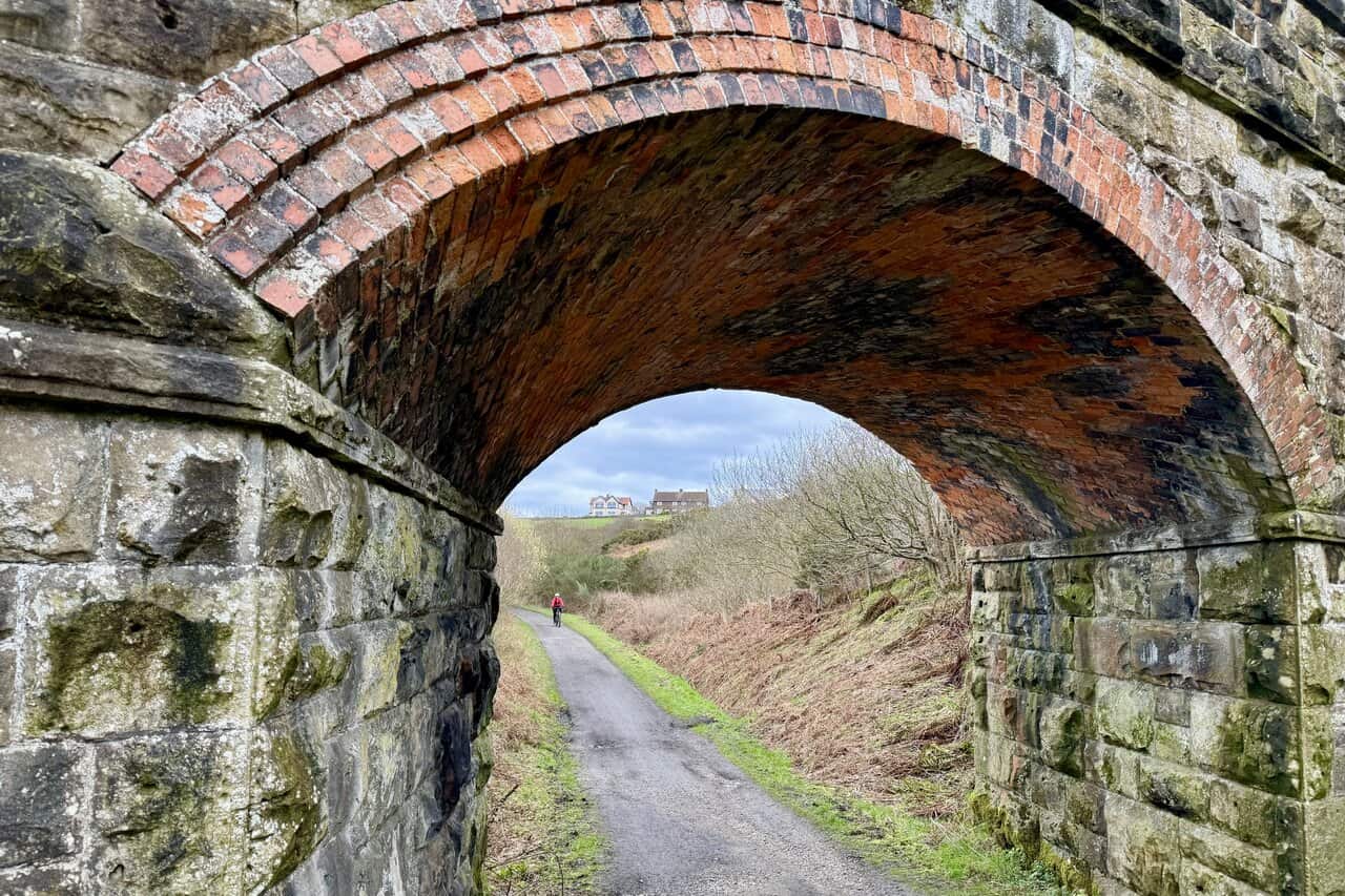 View through the final bridge on the Cinder Track, with a cyclist approaching and the houses on Raven Hall Road visible ahead. This almost completes the Ravenscar walk.