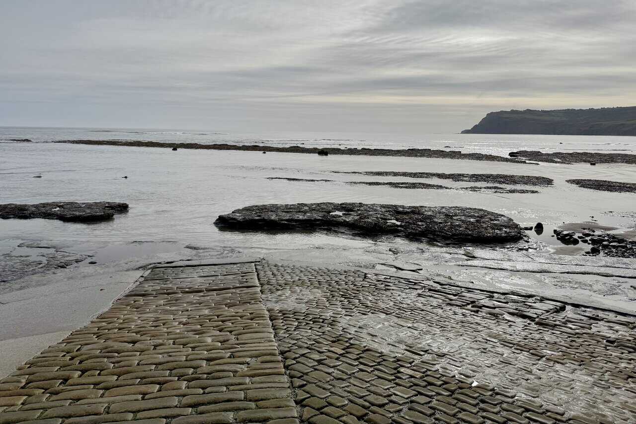 Cobbled slipway in Robin Hood’s Bay leading down to a rocky shore at low tide.