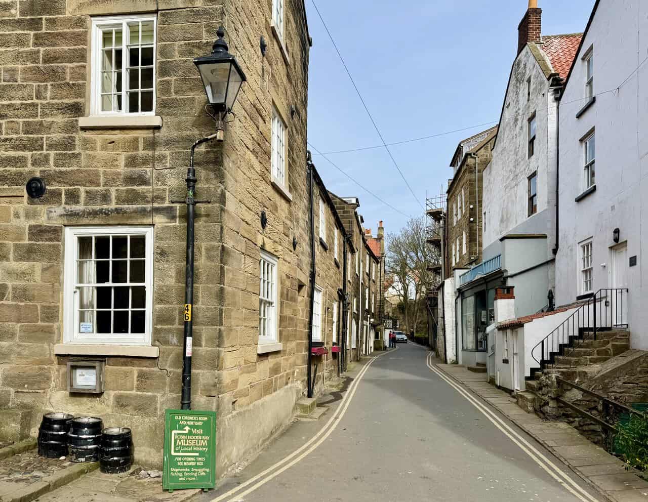 Narrow village street with museum sign, stone steps and old lamp posts in Robin Hood’s Bay.