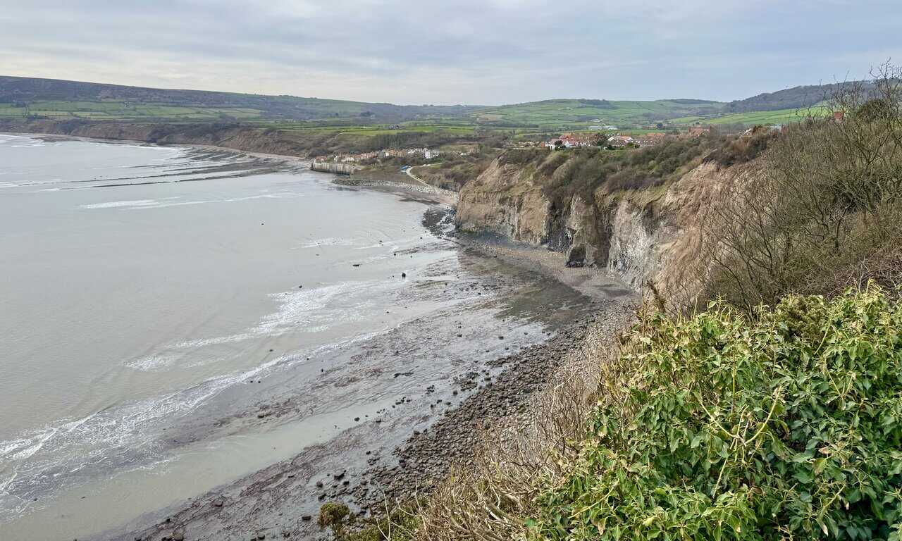 Panoramic view of Robin Hood’s Bay below steep cliffs and green farmland from the Cleveland Way.