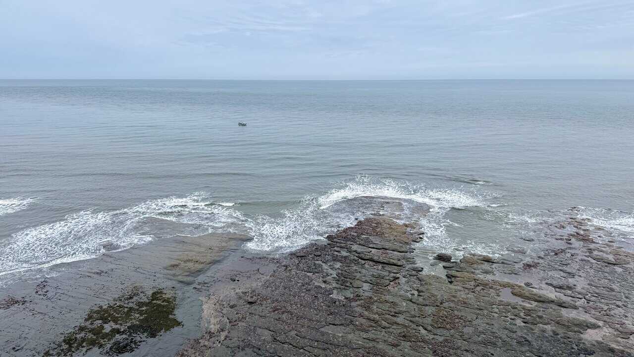 Fishing boat offshore beyond seaweed-covered rock platforms on the Robin Hood's Bay walk.