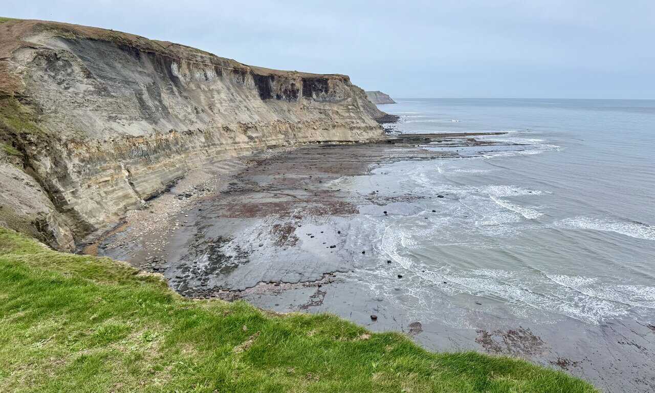 Layered cliffs above Far Jetticks with the sea washing across a wide flat shore.