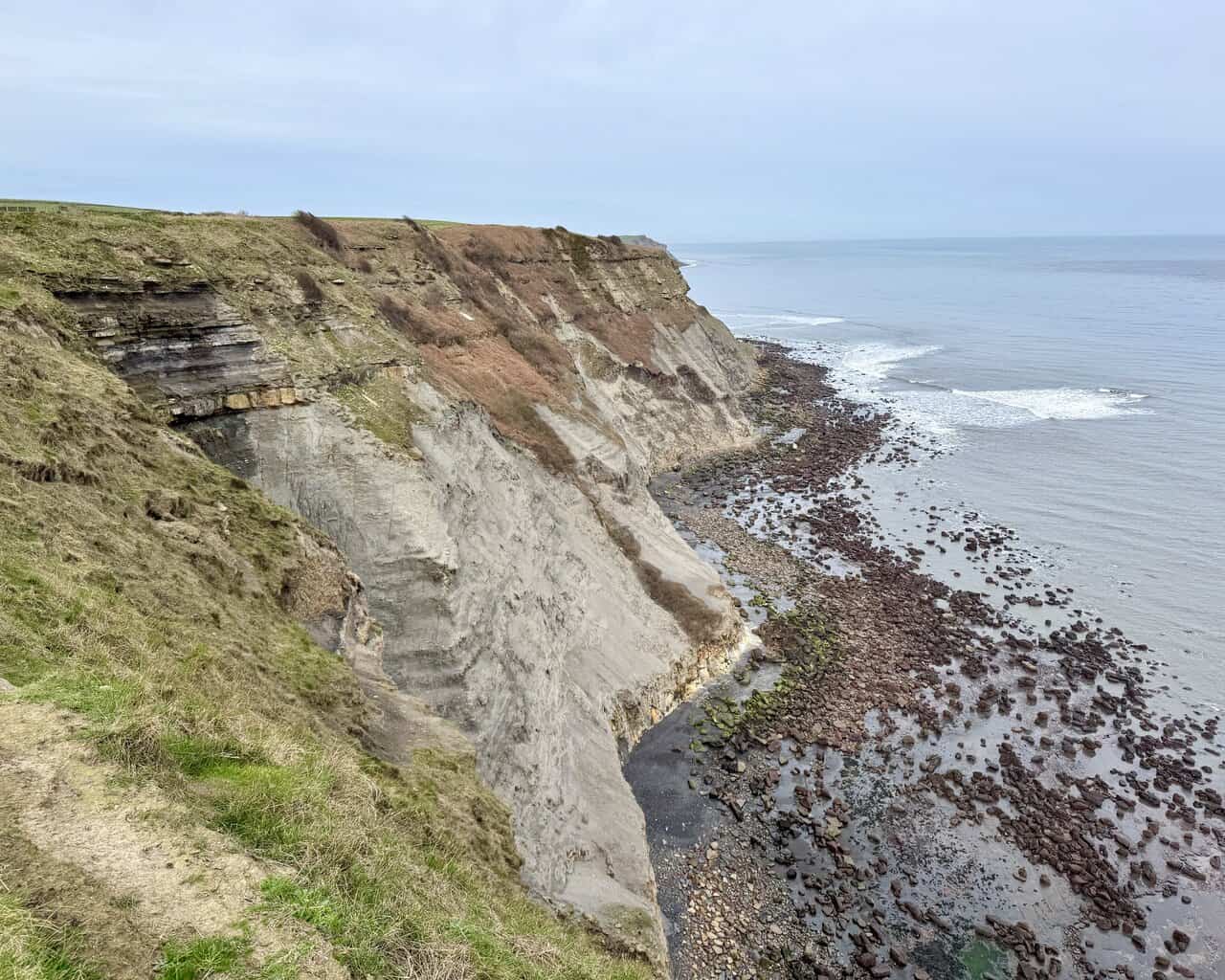 Heavily eroded cliffs and dark boulders stretching north towards Hawsker and Whitby.
