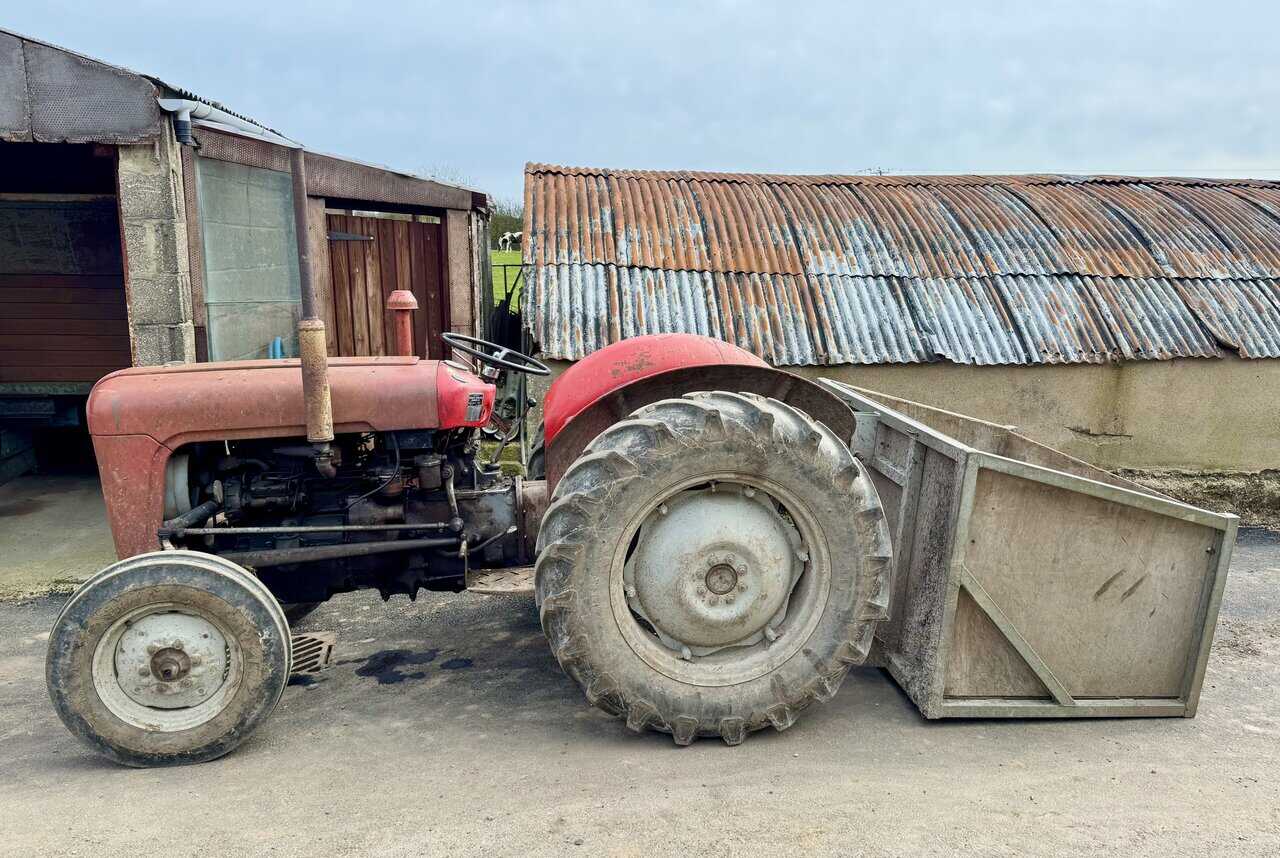 Old red Massey Ferguson tractor beside a corrugated barn and farm track.