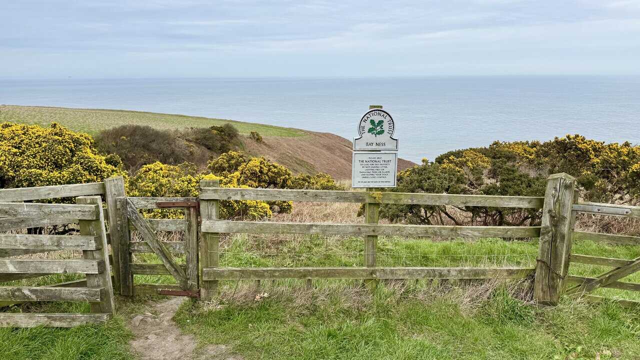 National Trust Bay Ness sign beside a wooden gate on the clifftop.