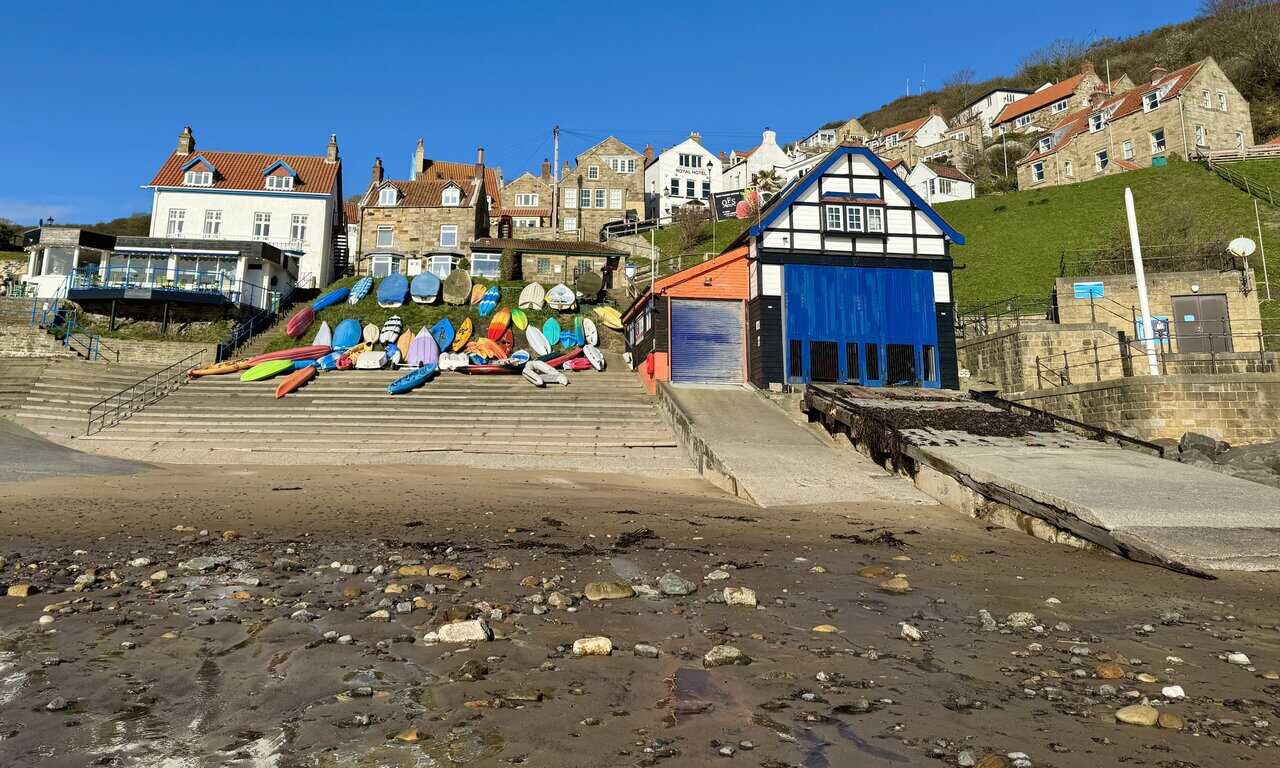 View up from Runswick Bay beach to the hillside village, where stone and rendered cottages rise in overlapping rows above the old lifeboat station.