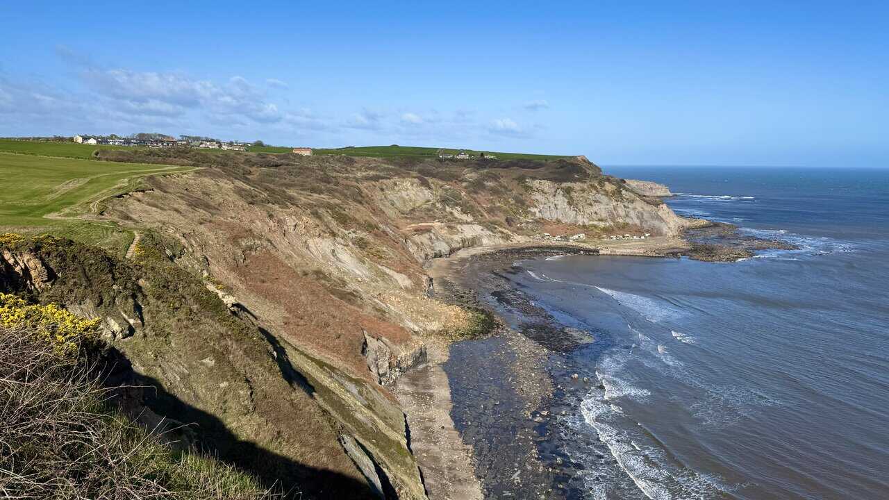 Layered Jurassic cliffs along Lingrow Cliffs, showing bands of ochre, grey and rust-coloured rock above the North Sea.