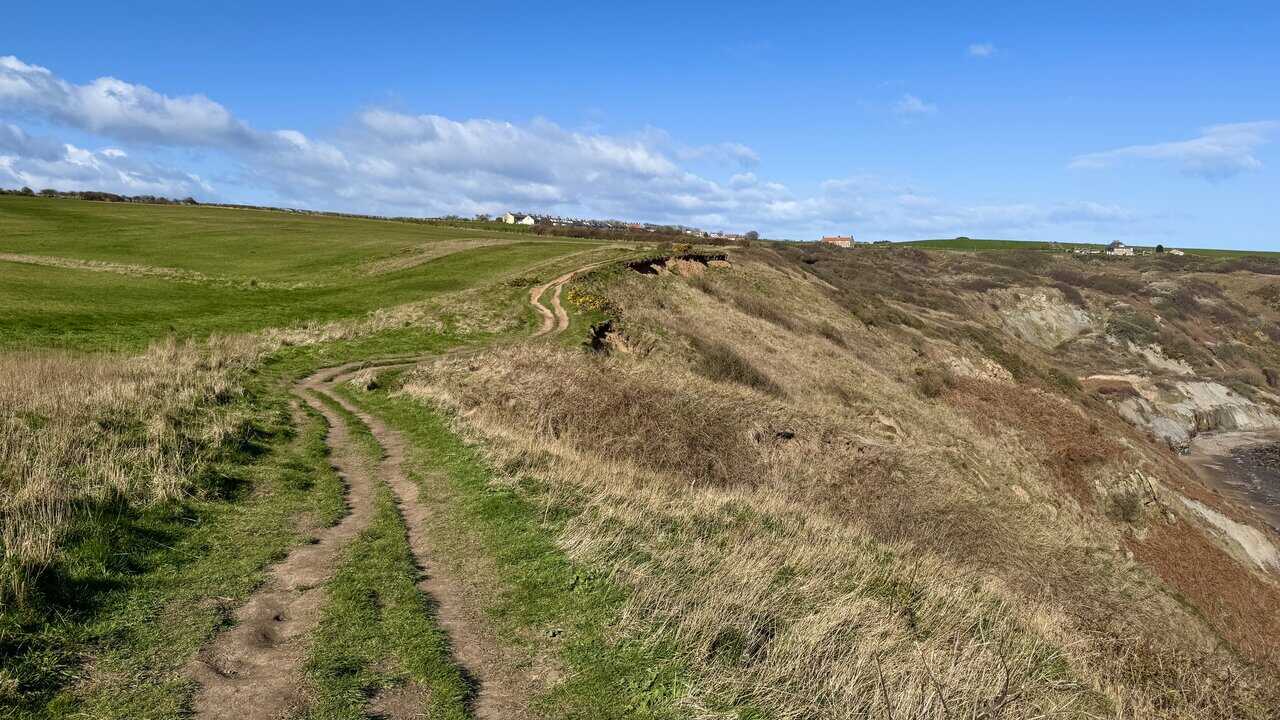 The Cleveland Way curving towards Port Mulgrave between farmland and the cliff edge, with the small bay and former harbour site below.