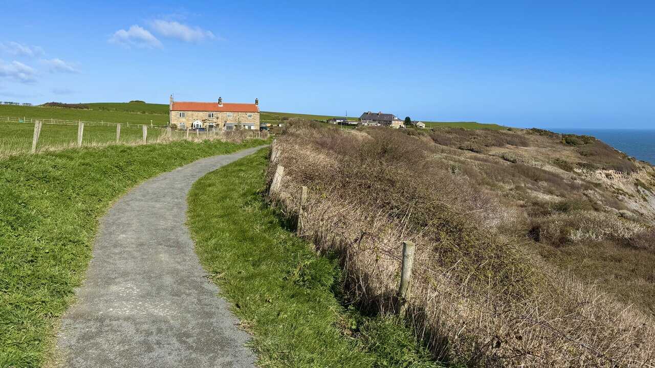 Clifftop path approaching Port Mulgrave, with scattered houses ahead and the coastline stretching towards the sea.