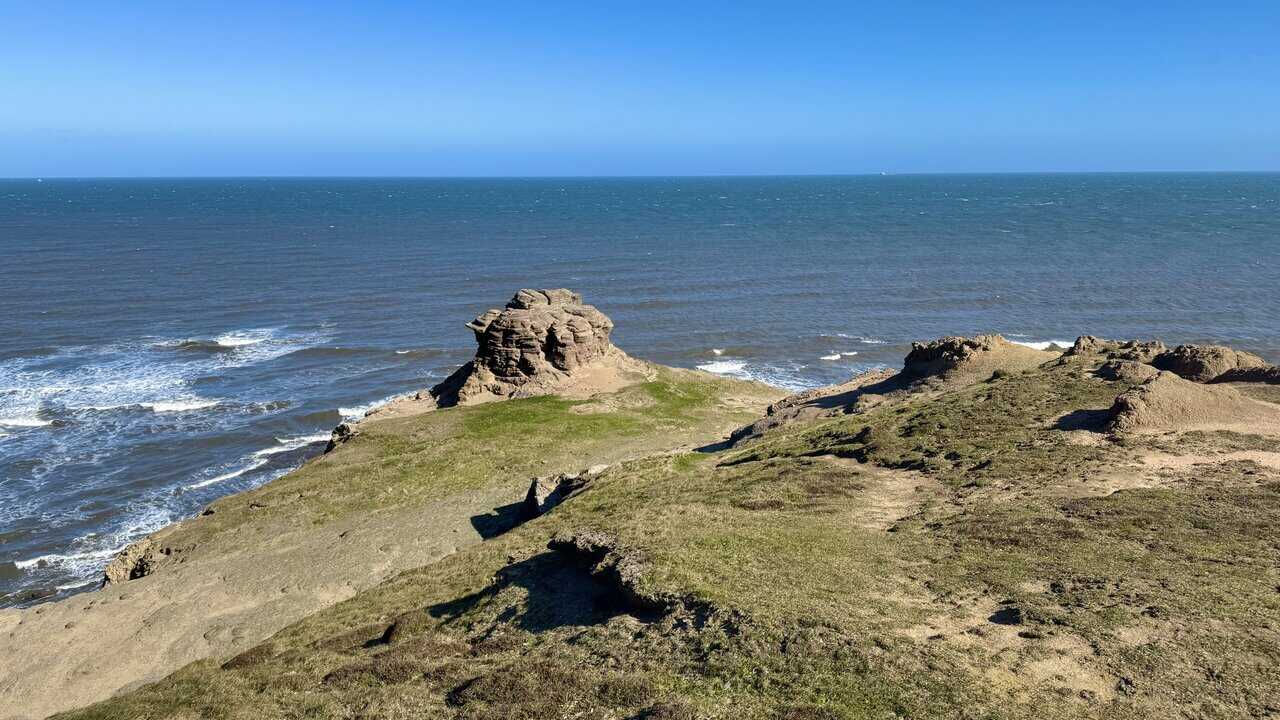 Weathered layered rock stack on the tip of Old Nab, standing alone on uneven, eroded ground above the sea.