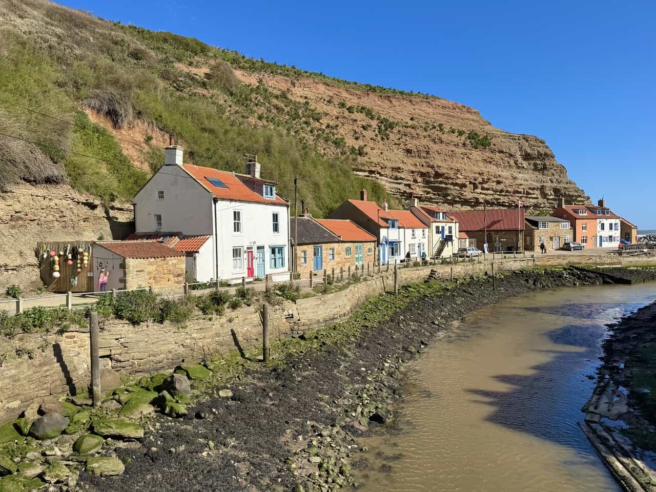 Footbridge over Staithes Beck leading to the Cowbar side, with brightly painted cottages, fishing gear and the exposed beck bed below.