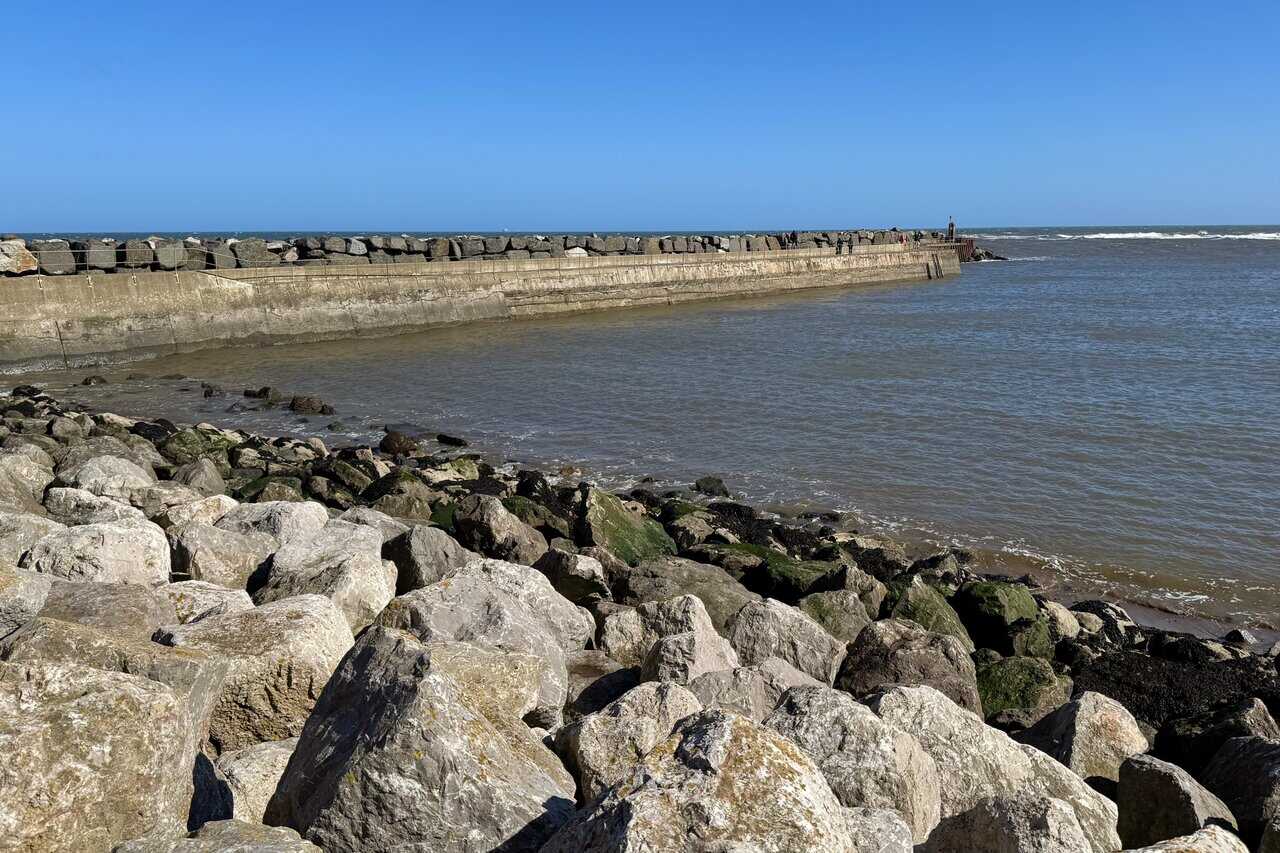 Concrete path towards the Staithes breakwater, bordered by heavy boulders and protective sea defences along the harbour edge.