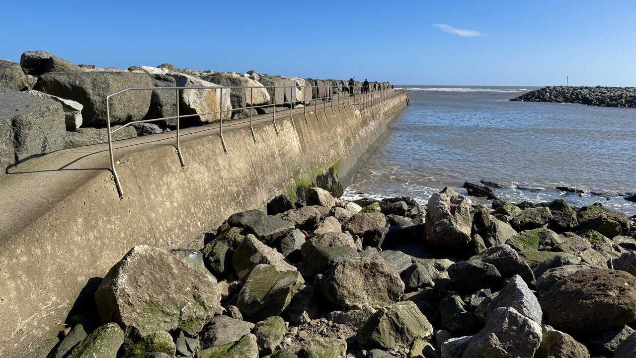 Staithes breakwater stretching out into open water, with metal handrails and walkers heading towards the far end.