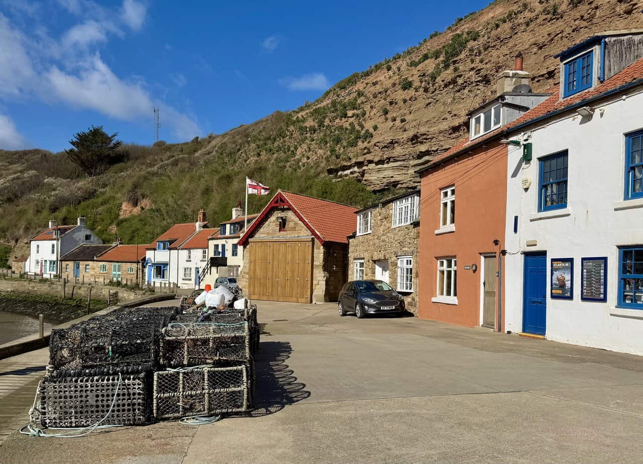 The RNLI lifeboat house on the Cowbar side of Staithes harbour, with stacked lobster pots and cottages nearby.