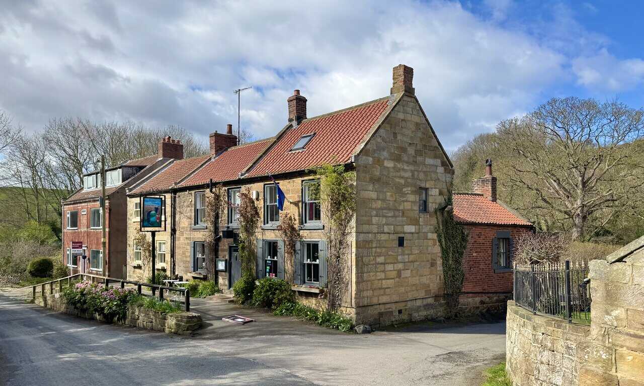 The Fox and Hounds at Dalehouse, a sandstone roadside pub with red pantile roofs and climbing plants on its walls.