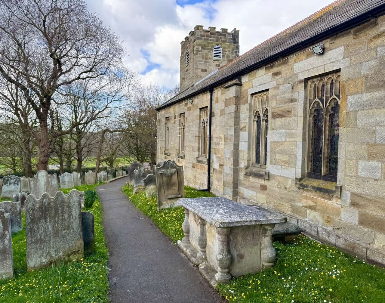 Path beside St Hilda’s Church passing weathered chest tombs and leaning gravestones in the churchyard.