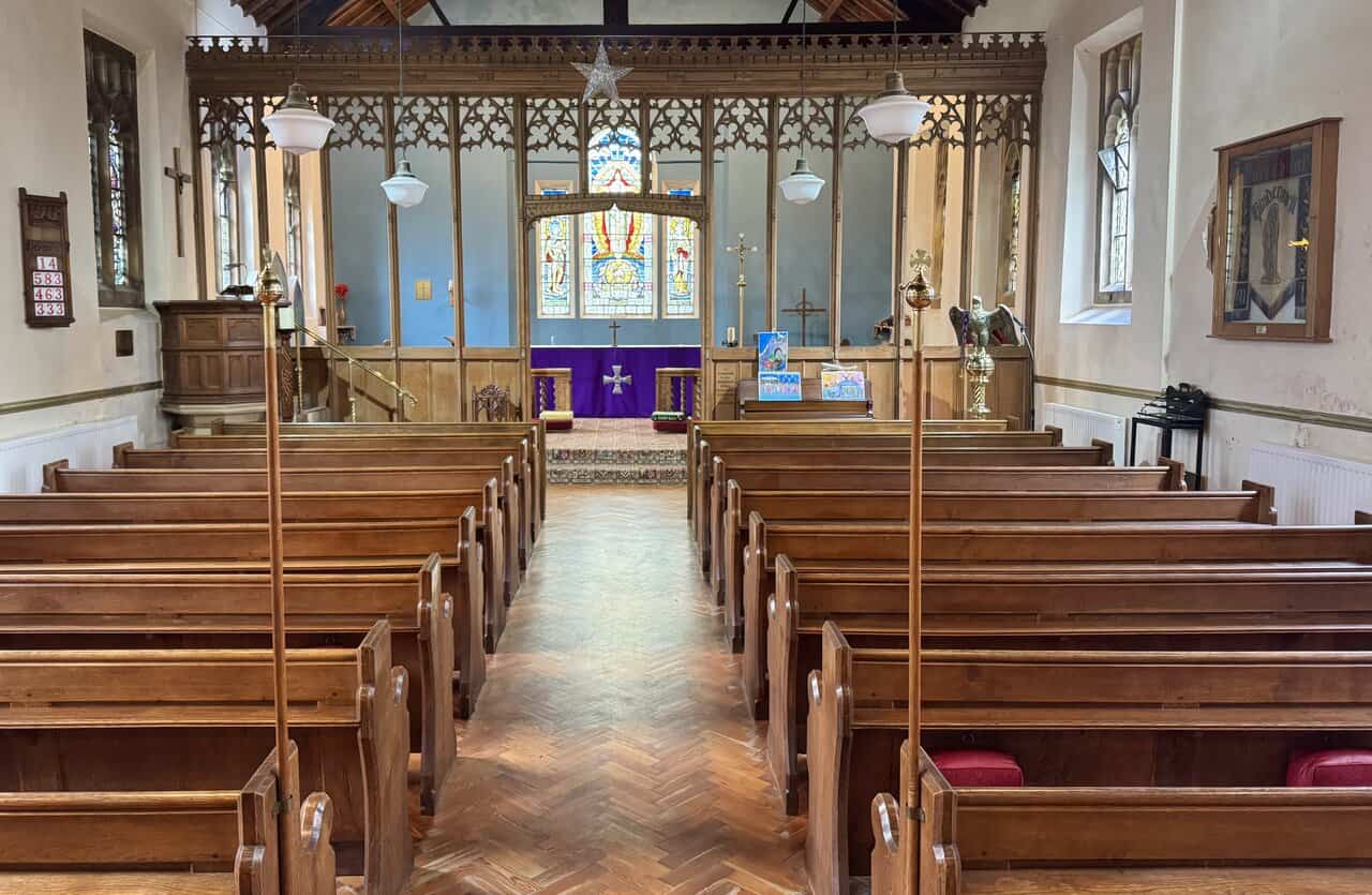 Interior of St Hilda’s Church, with oak pews, a herringbone floor, carved rood screen and blue-painted sanctuary beyond.