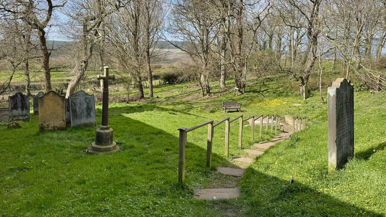 Stone steps descending through the churchyard towards St Hilda’s Well, passing a stone cross and old headstones.
