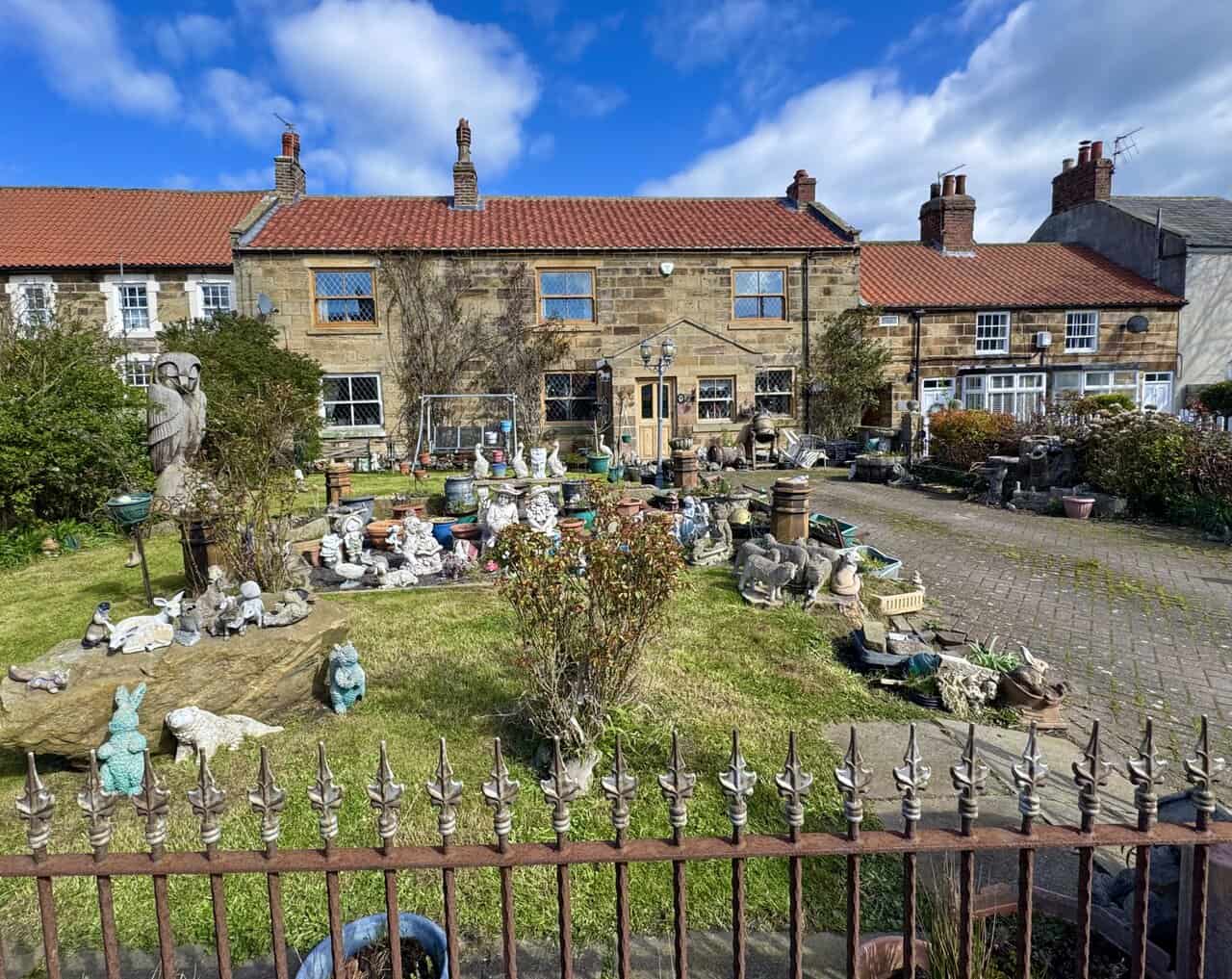 Sandstone cottage in Hinderwell with leaded windows and a front garden crowded with ornaments, pots, carvings and a large wooden owl.